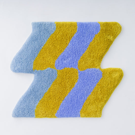 青、黄色、紫の3色で構成されたジグザグ模様のタフティングラグ。デザインは曲線的で、カラフルでポップな印象を与える。滑らかでふわふわとした質感が特徴