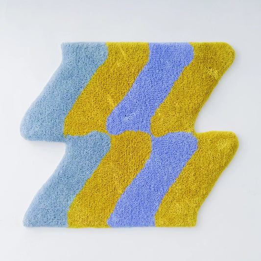 青、黄色、紫の3色で構成されたジグザグ模様のタフティングラグ。デザインは曲線的で、カラフルでポップな印象を与える。滑らかでふわふわとした質感が特徴