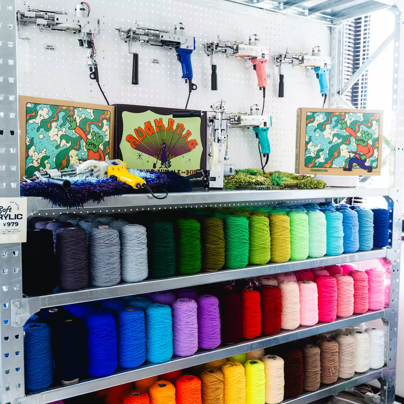 壁に掛けられたカラフルなタフティングガンと、その下に飾られたアートボードやマット