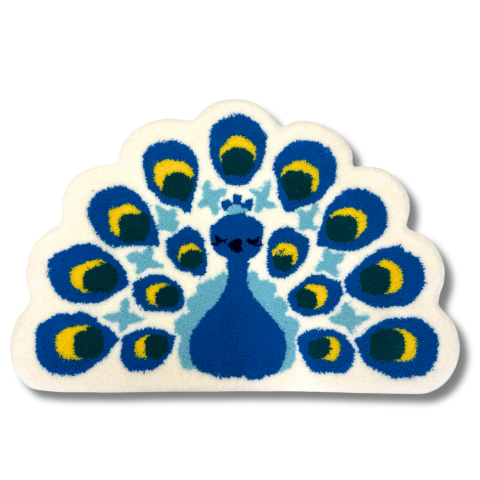 孔雀をモチーフにした半円形のラグ。白地に青い体と鮮やかな羽根模様が描かれており、羽根には黄色と緑がアクセントとして入っている。