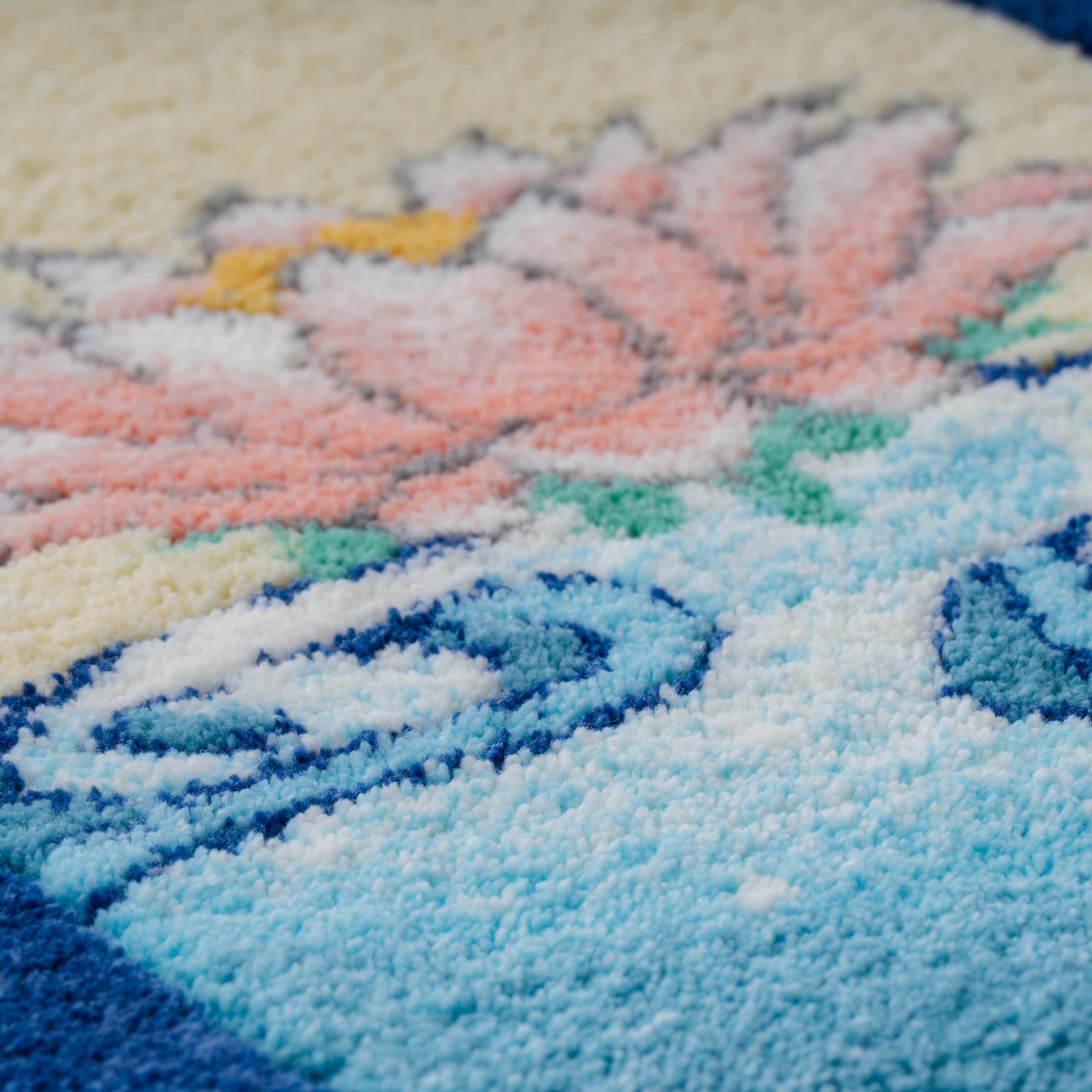 ブルーの水面と淡いピンクの花を毛糸で描いたタフティングラグの接写。細かなパイルの高さと色の階調で柔らかな世界観を表現したアートラグ。RUGMATAGの精密なタフティング技術を伝えるディテール写真