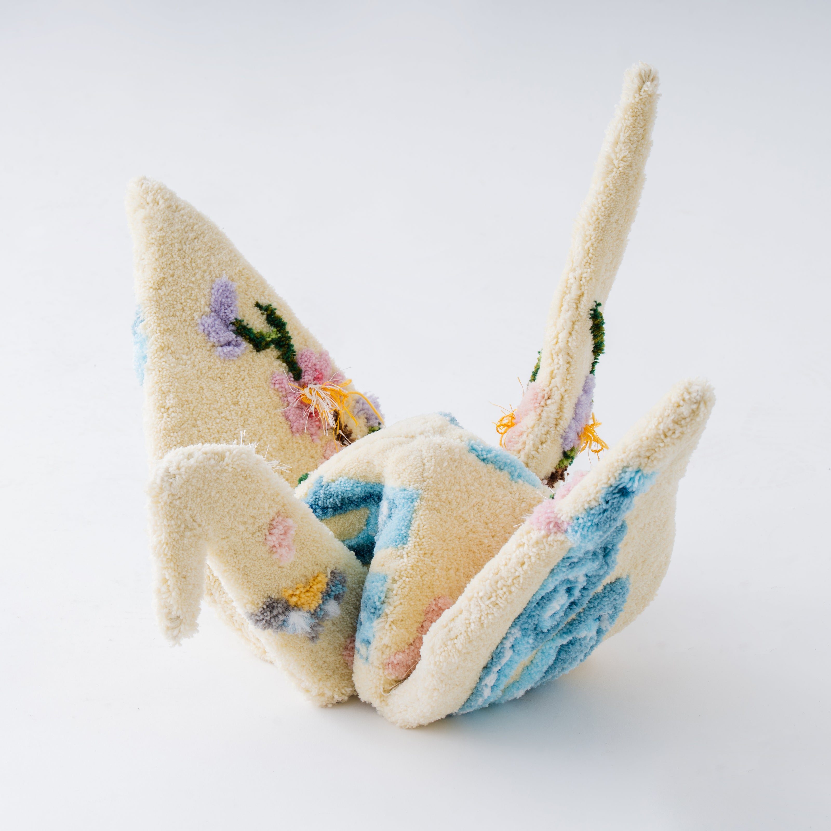 淡いクリーム×パステルカラーで仕上げたタフティングの立体折り鶴作品。花柄と柔らかな色合いが特徴で、毛糸で折り紙の造形を表現したアートオブジェ。RUGMATAGの立体タフティング技法を活かした作品。