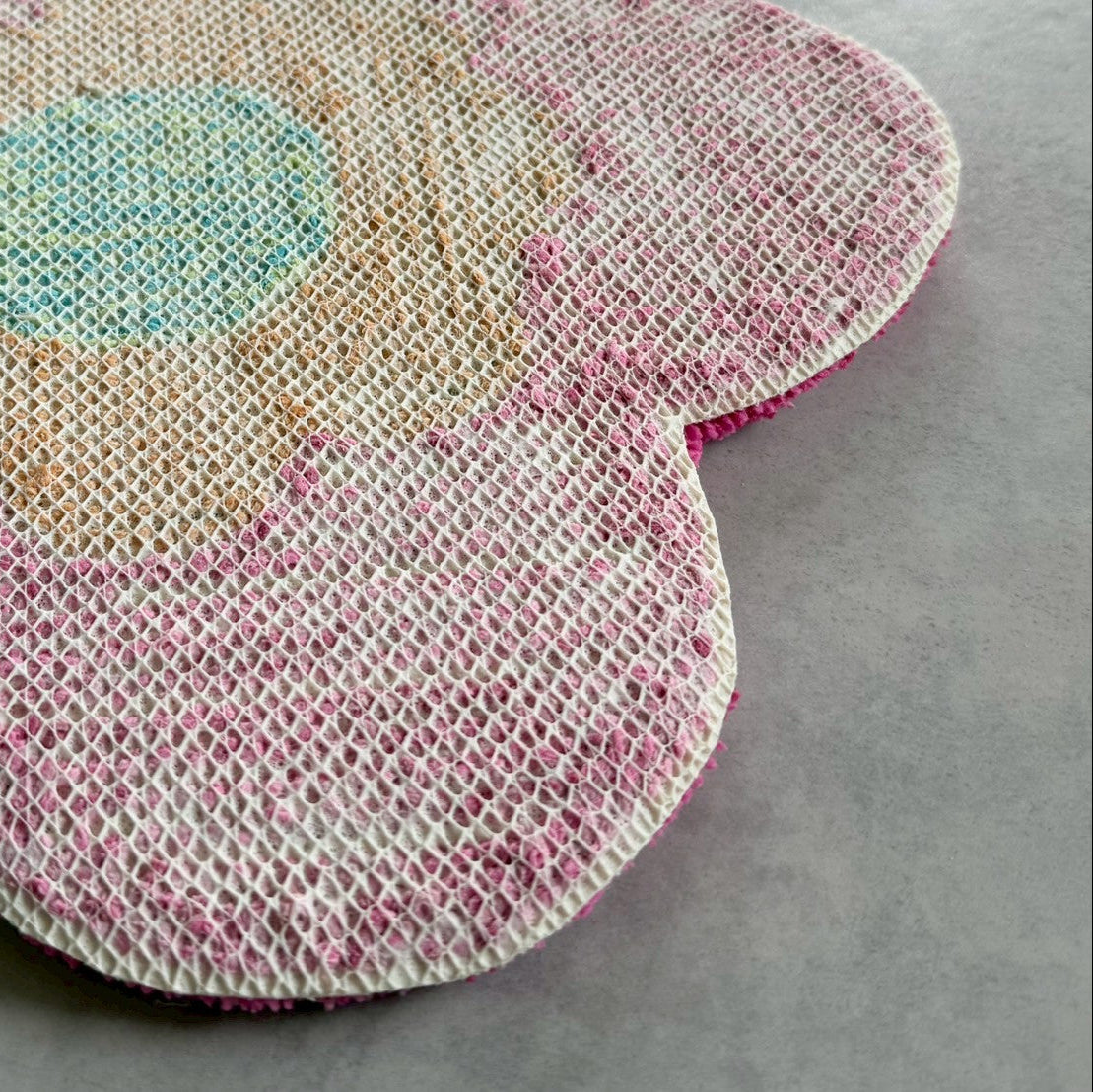 花型ラグの裏面に滑り止め加工されたメッシュバッキングが見える。