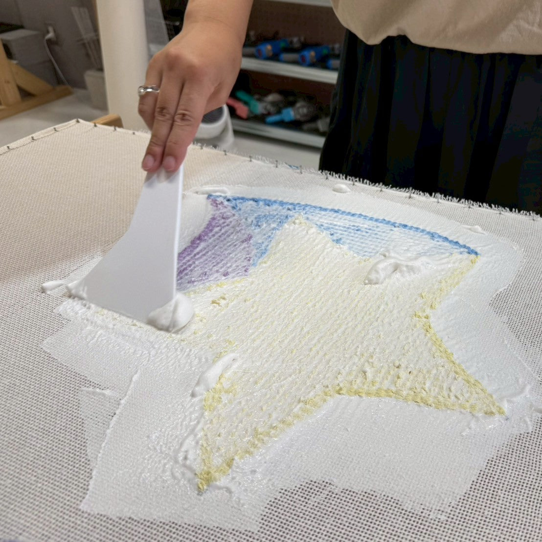 星型ラグの裏面に白い接着剤をヘラで均等に塗布している。