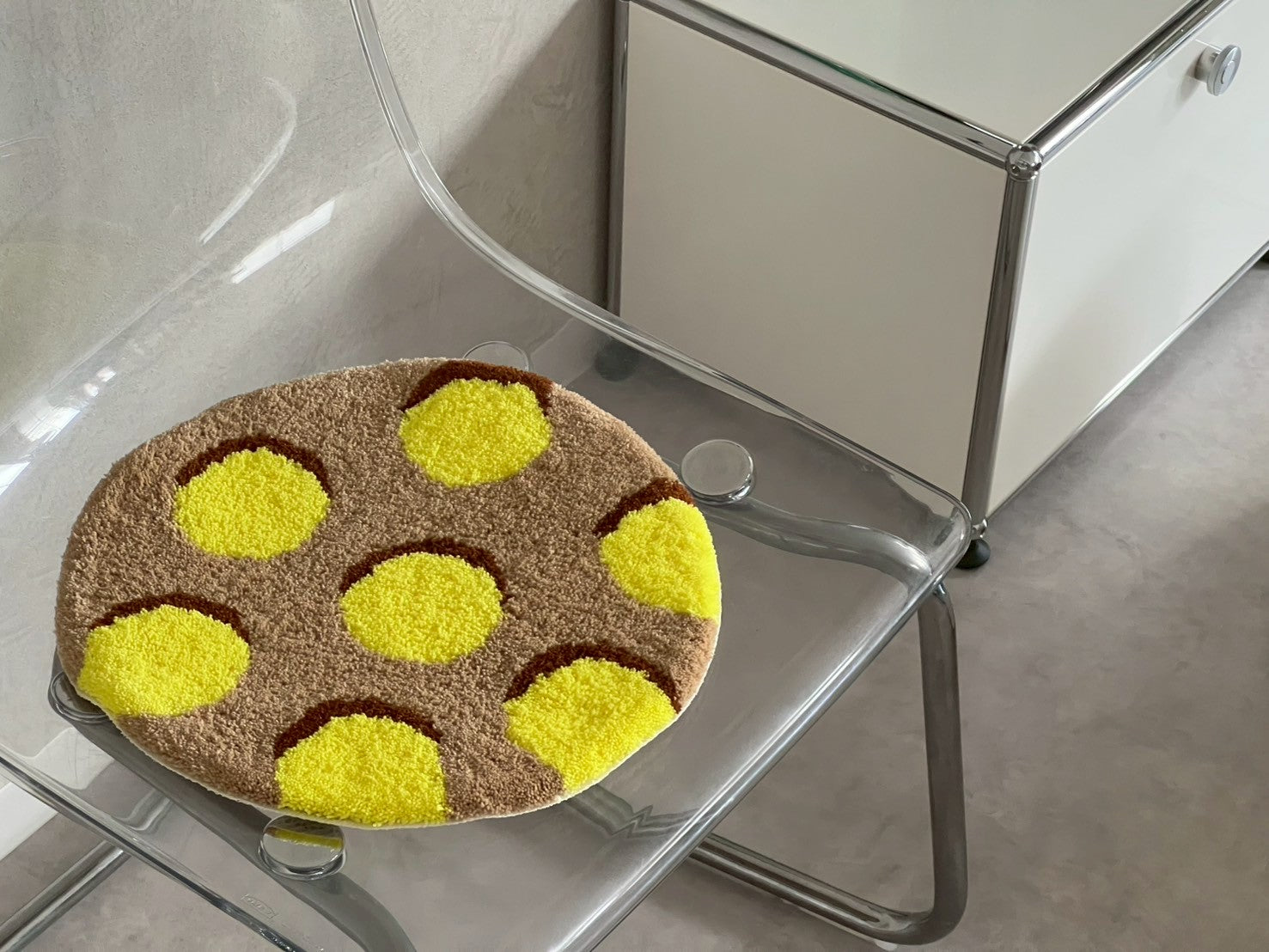 透明な椅子に置かれた円形のタフティングラグ。茶色のベースに明るい黄色の水玉模様がデザインされている。チェア&アートラグコース タフティングワークショップ 大阪北堀江