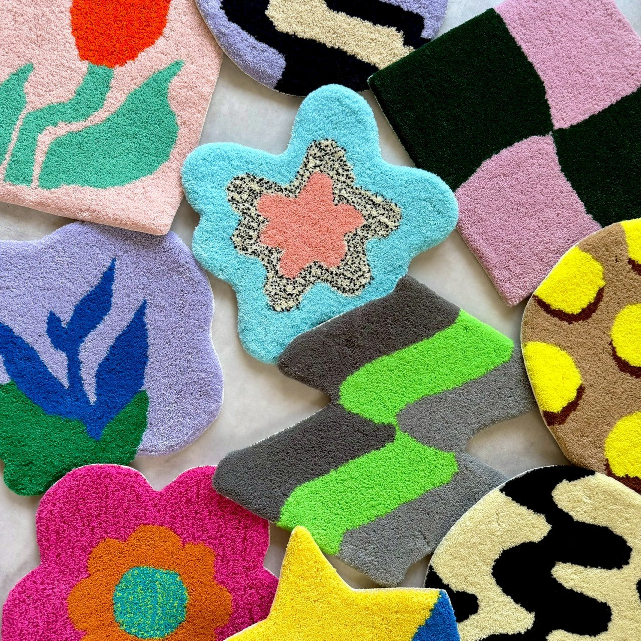 床に並べられた複数のタフティングラグ。星、花、チューリップ、幾何学模様など、さまざまな形とカラフルなデザインが散らばっている。チェア&アートラグコース タフティングワークショップ 大阪北堀江