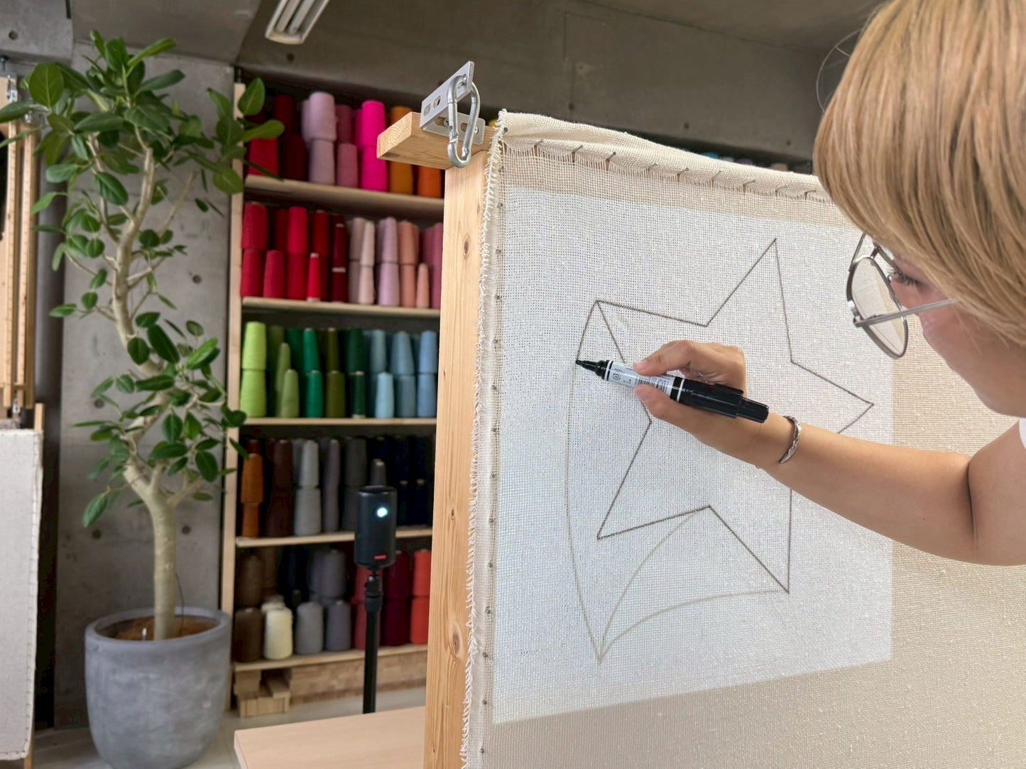 プロジェクターを使用して基布に黒いペンで大きな星型のデザインを描く人物。チェア&アートラグコース タフティングワークショップ 大阪北堀江
