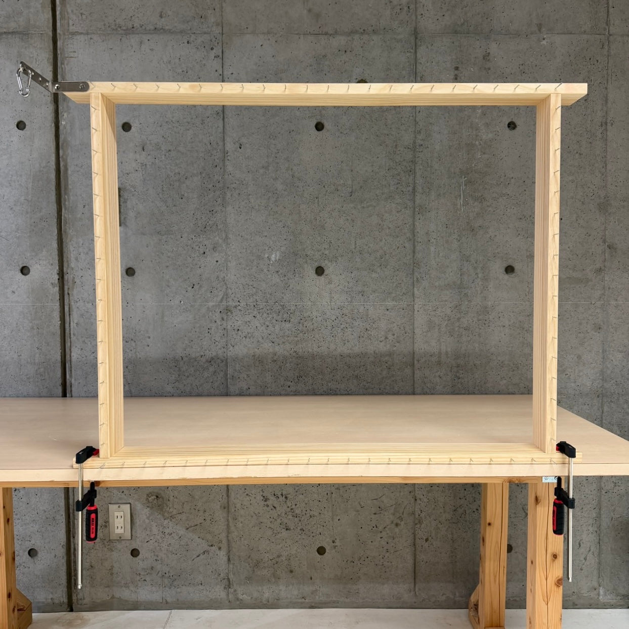 【MIYOSHI RUG職人監修】木製テーブルにクランプで固定した横長のタフティングフレーム。周囲に釘が打たれ、左上に糸ガイド用の金具とカラビナが付いた全体写真。