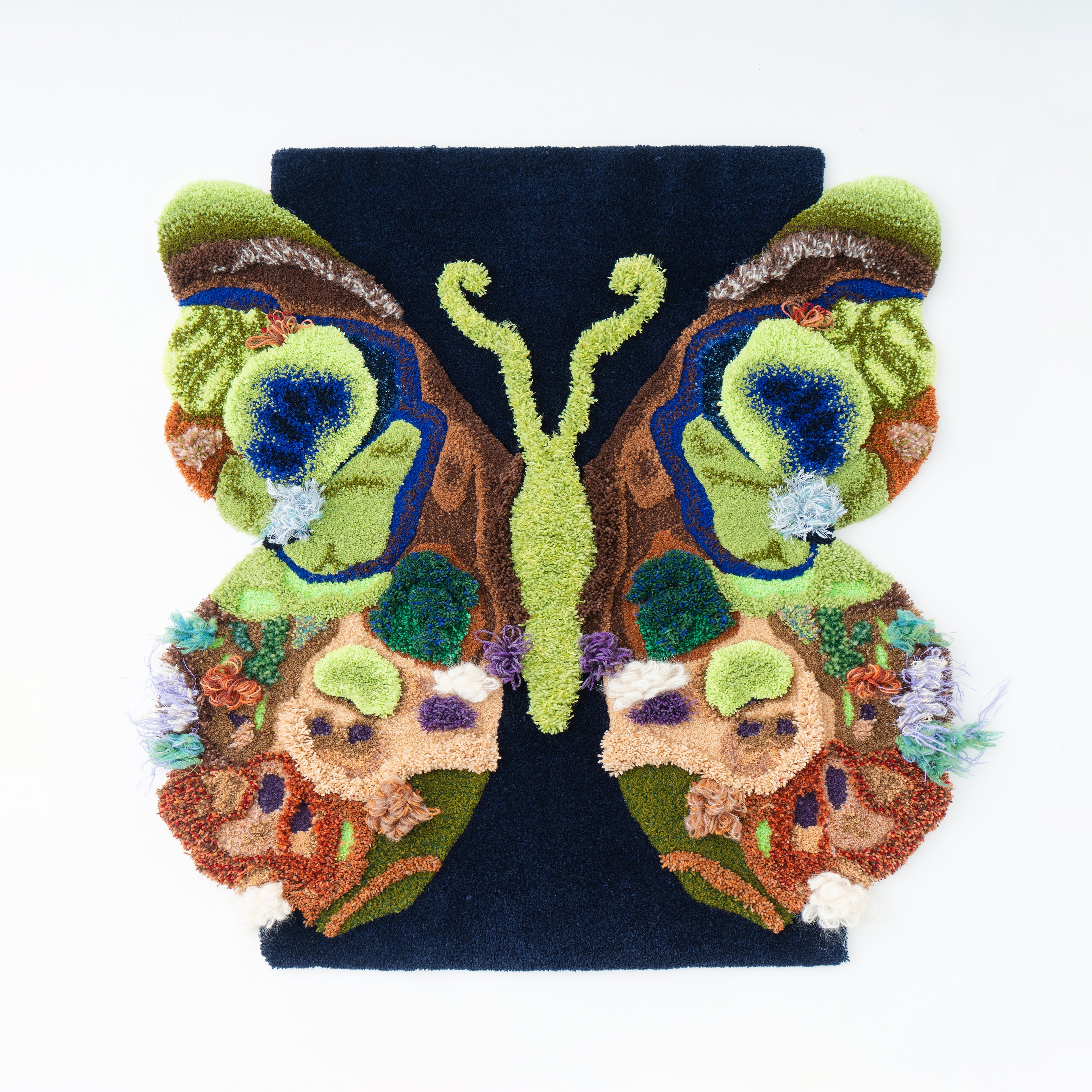 多彩な毛糸の質感と立体的なテクスチャーで表現された蝶のタフティングラグ作品。グリーンやブルー、ブラウンを基調にした左右対称デザインが特徴のアートラグ。RUGMATAGの高密度タフティング技術を活かしたインテリアアート