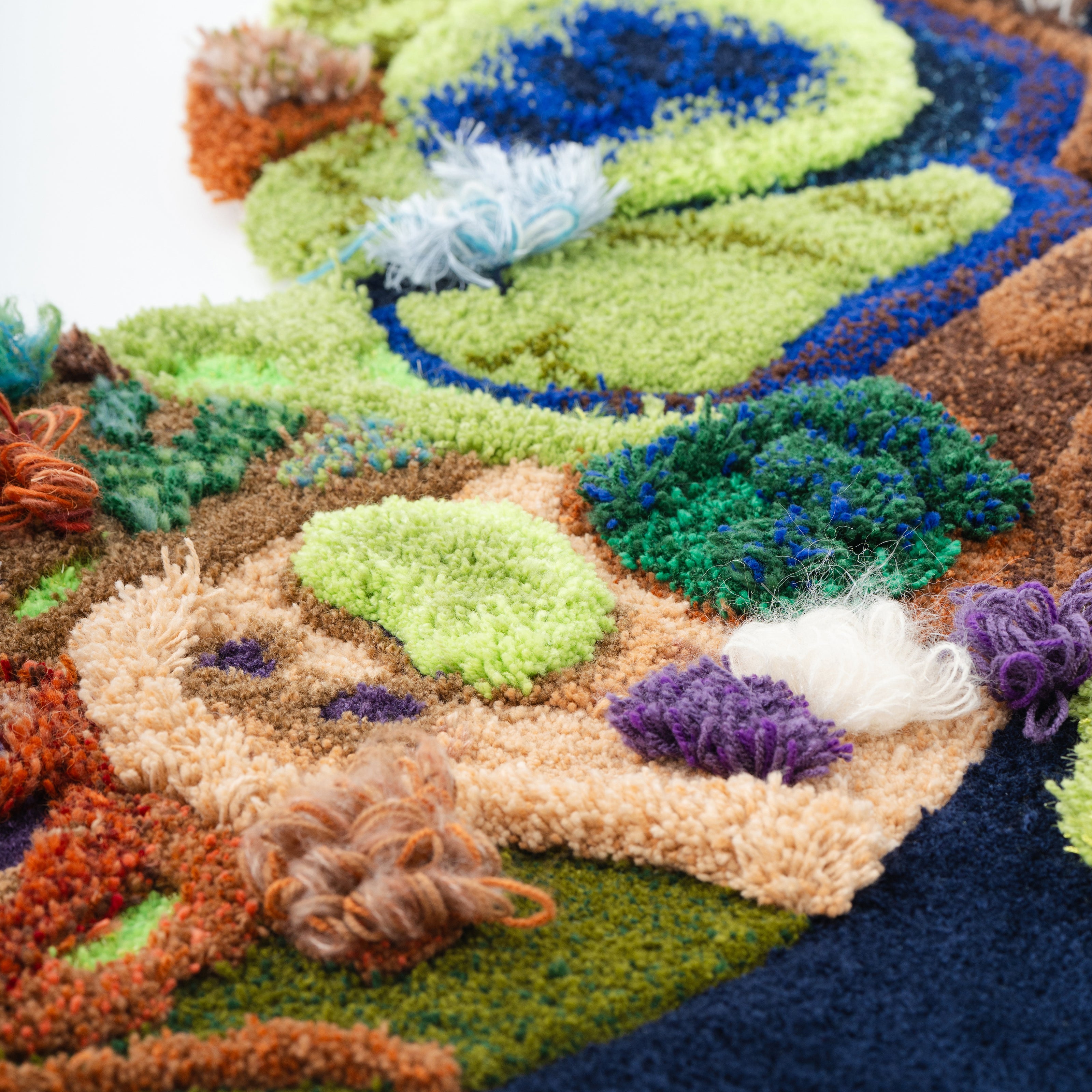 多彩な毛糸の質感と立体的なテクスチャーで表現された蝶のタフティングラグ作品。グリーンやブルー、ブラウンを基調にした左右対称デザインが特徴のアートラグ。RUGMATAGの高密度タフティング技術を活かしたインテリアアート