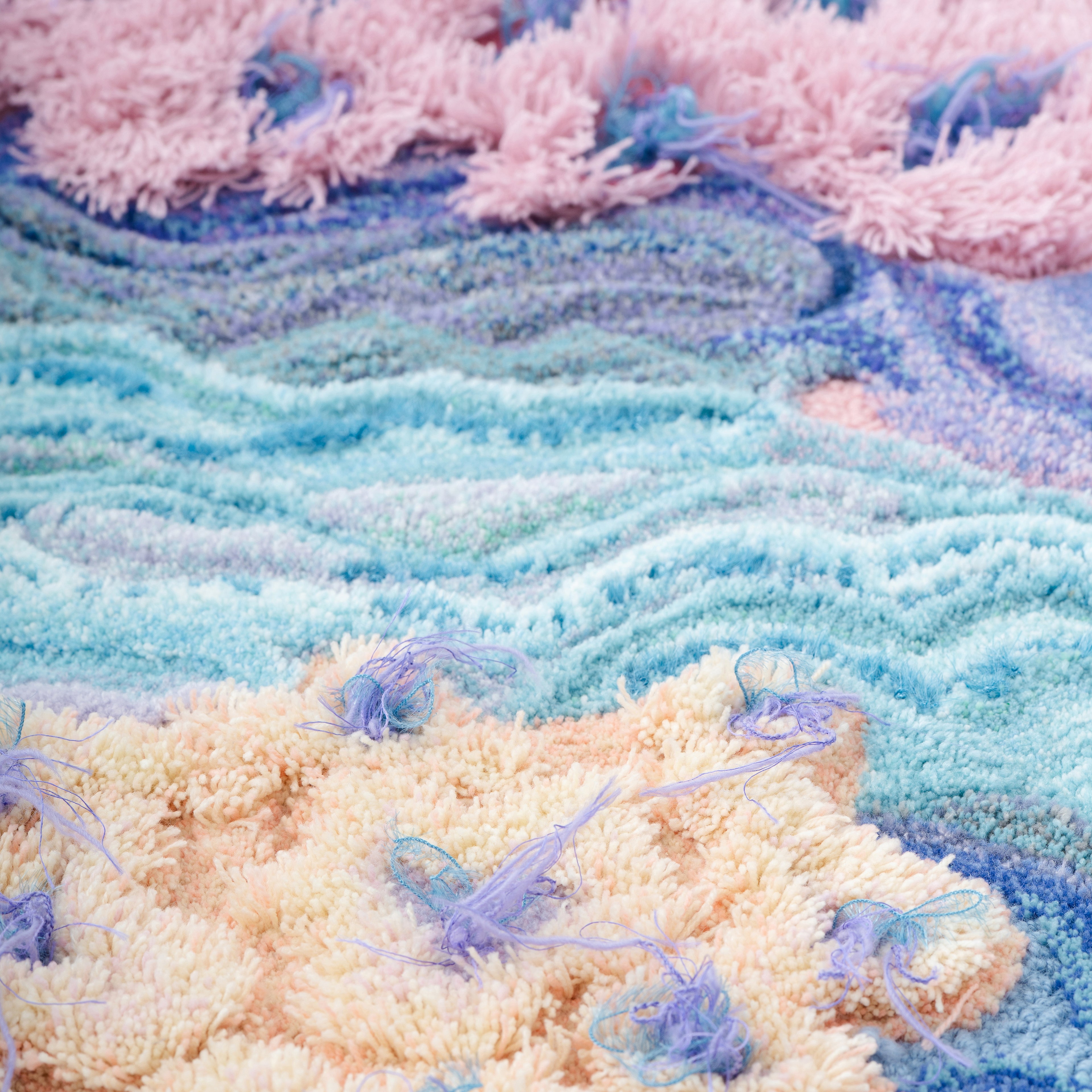 ピンクやブルーの毛糸を使ったタフティングラグの凹凸テクスチャーを写した接写画像。繊細なカットパイルとループパイルが重なり、立体感のある表面表現を確認できるディテール写真。RUGMATAGの素材感を伝えるクローズアップ